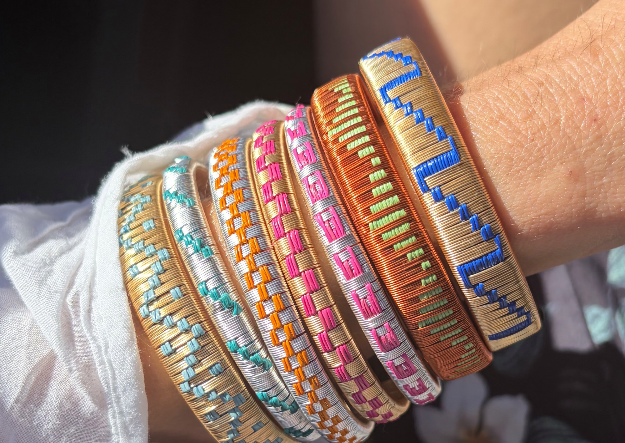 Seven woven bangles stacked on a wrist, gold and silver with coloured patterns